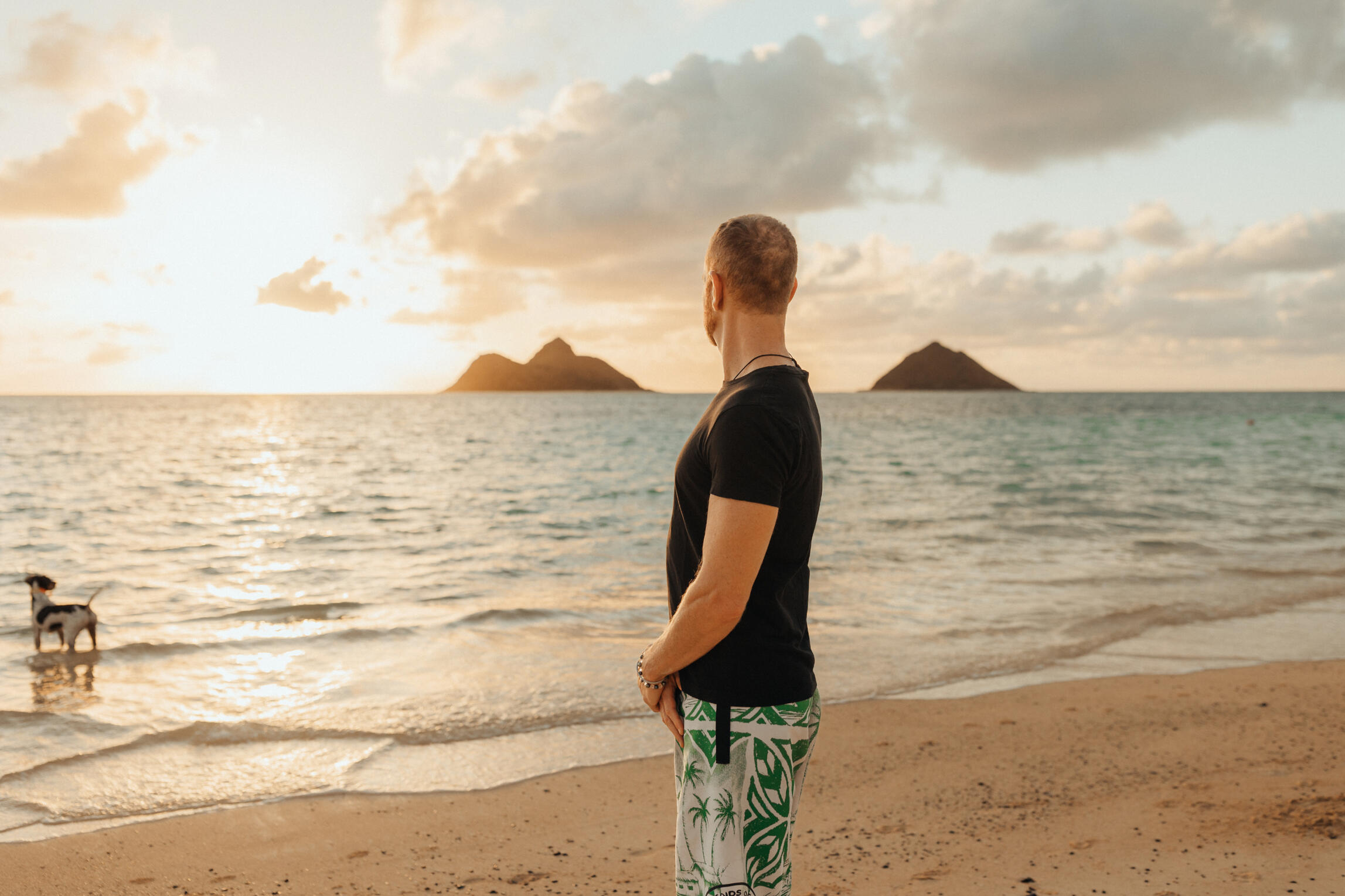 Image of Jay from Mokulua Massage stating on the beach peacefully looking out to the sunset.